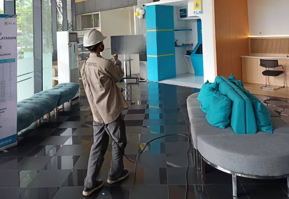 Teknisi pest control profesional sedang melakukan penyemprotan di lobi gedung perkantoran modern.